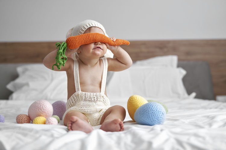 Girl covering eyes with toy while playing on bed