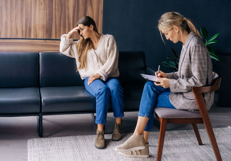 An upset woman in an emotional crisis sitting on a couch and a psychotherapist consultant 