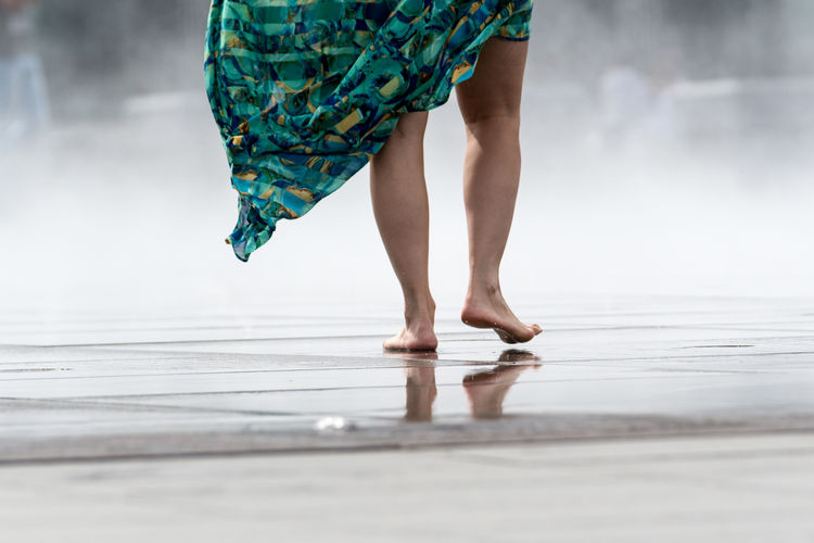 Low section of woman walking on wet walkway by fountain