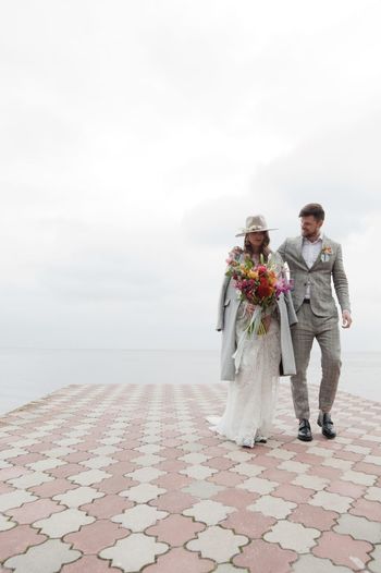 Newly married couple walking on pier over lake against cloudy sky