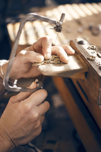 Cropped image of female goldsmith using saw while making jewelry in workshop