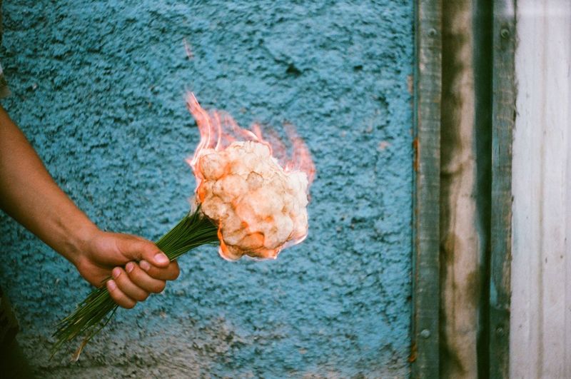 Cropped hand holding burning bouquet against blue wall