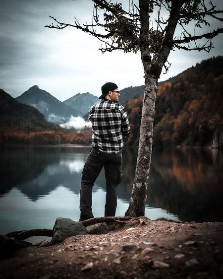 Full length of young man standing outdoor by lake against mountains and sky