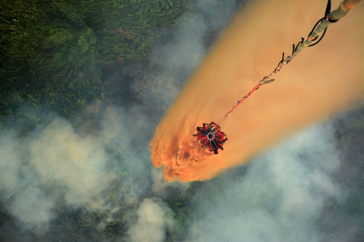 High angle view of retardant falling from container over forest fire