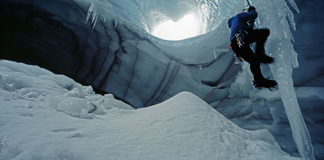 Ice climber scaling icicle in cave underneath langjokull glacier
