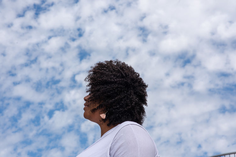 Low angle view of woman with curly hair against cloudy sky