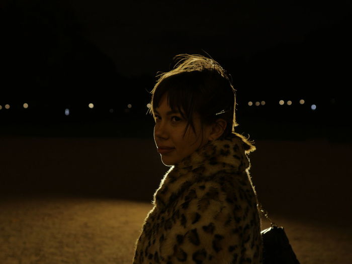 Portrait of woman looking at illuminated camera at night