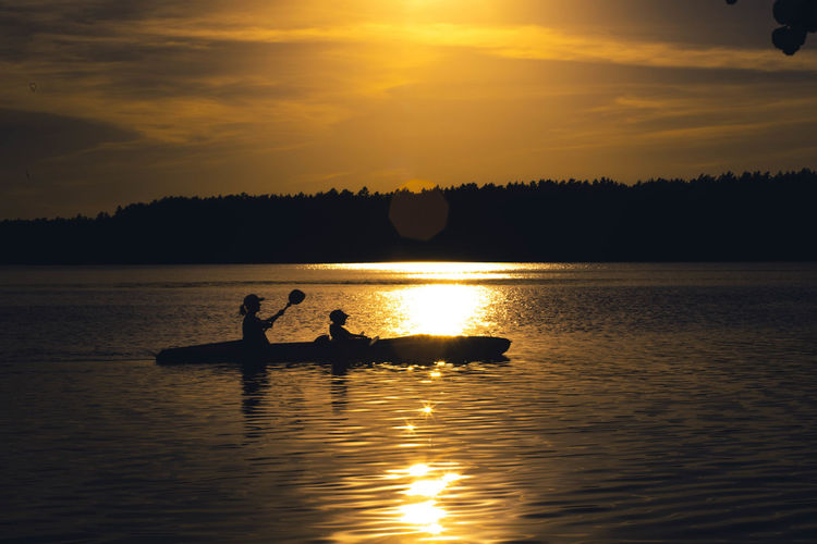 Two people are kayaking, sunset in the background