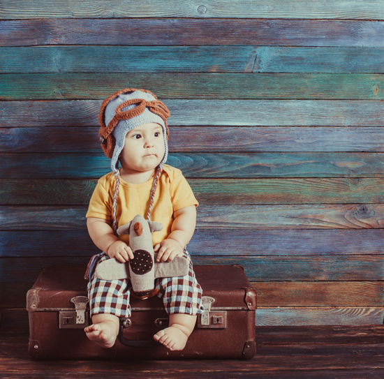 Full length of cute baby boy sitting against wooden wall
