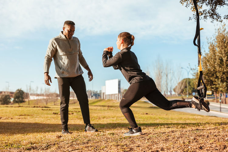 Full length of man assisting friend in exercising at public park