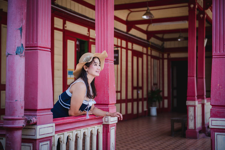 Woman wearing hat looking away while standing by railing