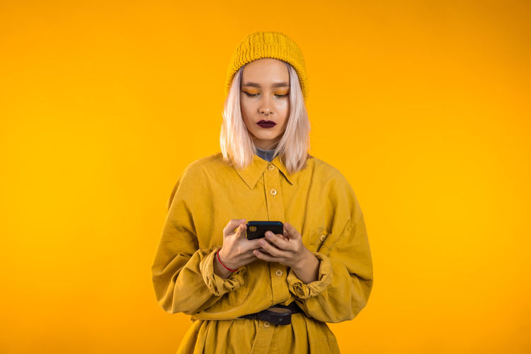 Young man using mobile phone against yellow background