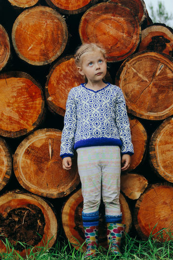 Rustic style, a girl in casual clothes sits on a bench against the background of a woodpile
