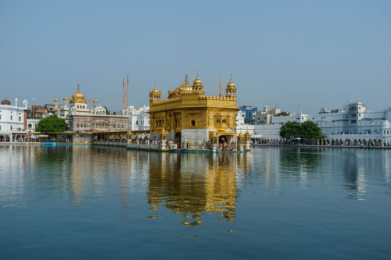 Reflection of golden temple in lake against clear sky