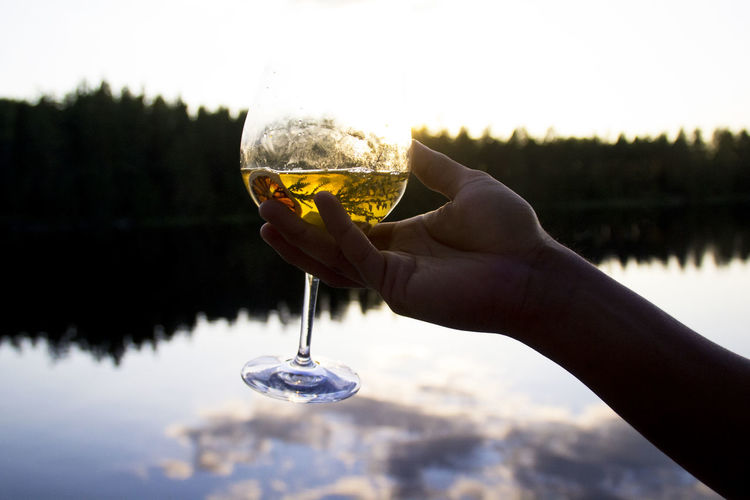Close-up of hand holding drink against lake