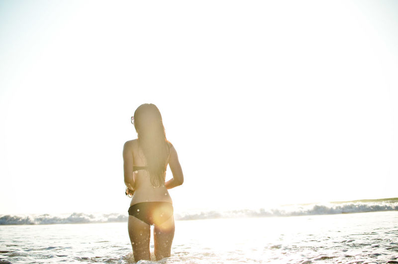 Rear view of woman in bikini enjoying in sea on sunny day