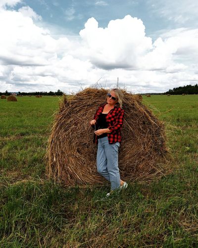 Full length of woman standing by haystack at farm against sky