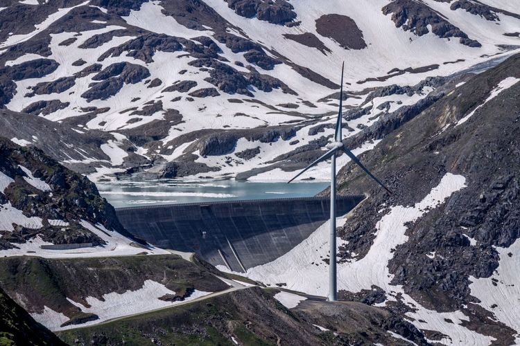 High angle view of snowcapped mountain with hydroelectric dam and wind turbine