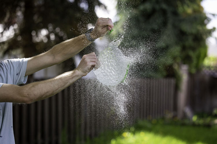 Midsection of man bursting water bomb in yard