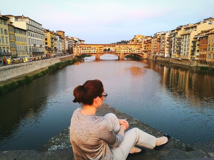Woman sitting by arno river against ponte vecchio