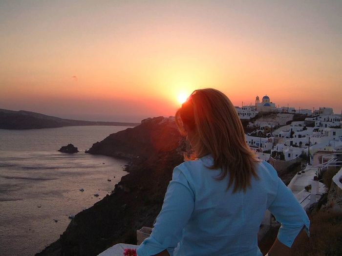 Rear view of woman by sea during sunset at santorini