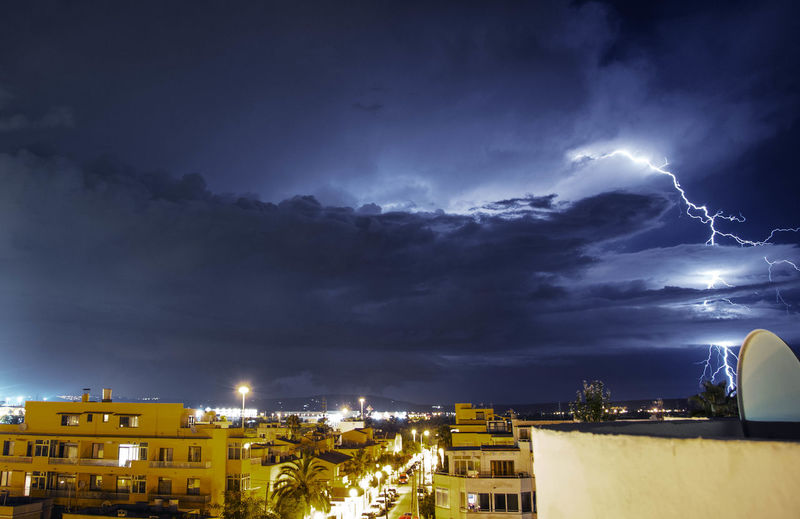 Lightning over cityscape against sky at night