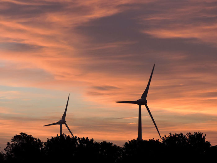 Silhouette wind turbines on field against cloudy sky during sunset
