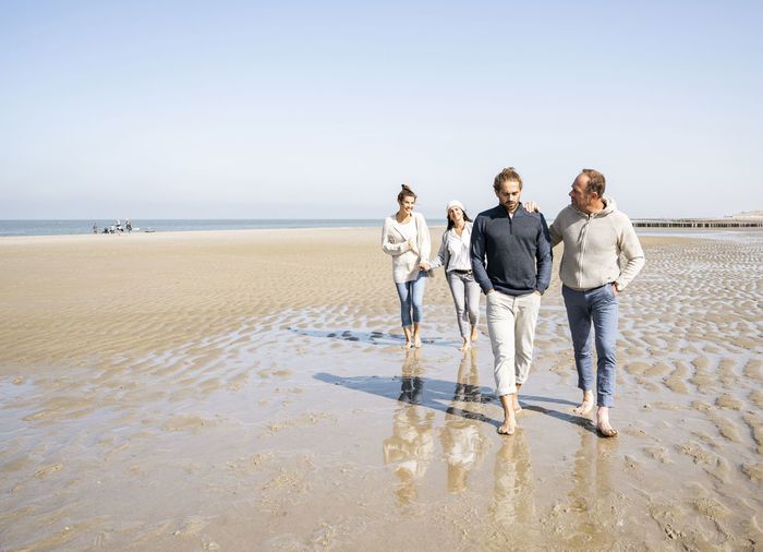 Men walking with women standing in background at beach