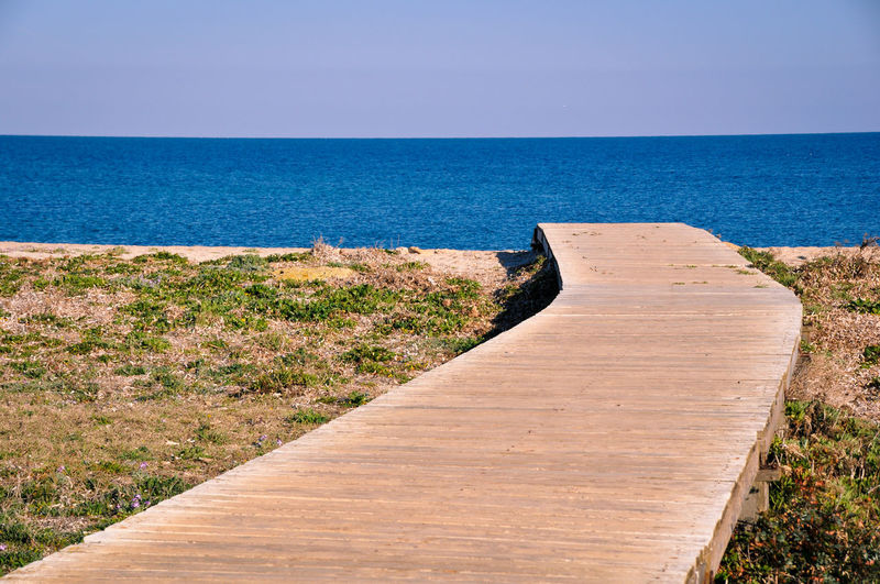 Footpath by sea against clear sky