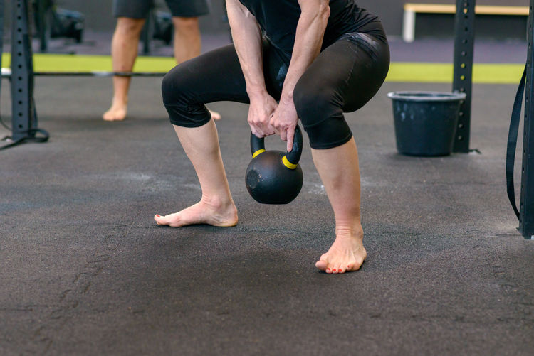 Low section of female athlete exercising with kettlebell in gym
