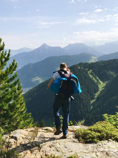 Rear view of man with backpack standing in cliff against mountain range