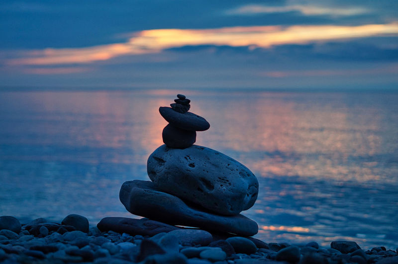Stone stack on rock at beach against sky during sunset