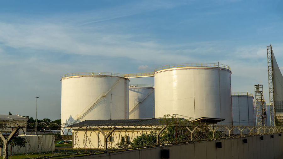 Low angle view of factory fuel tanks against sky