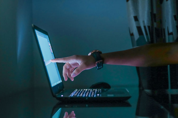 Cropped hand pointing on laptop screen at home