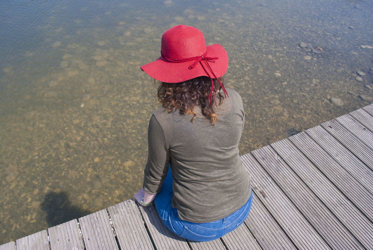 Rear view of woman sitting on pier over water