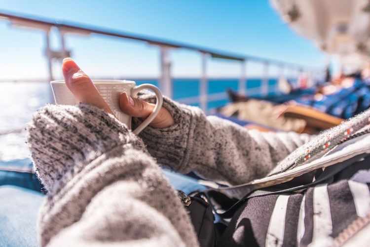 Midsection of woman holding cup while relaxing on cruise ship
