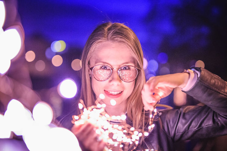 Portrait of smiling young woman holding illuminated lights