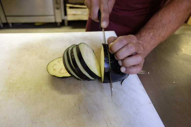 Midsection of man slicing eggplant on kitchen counter