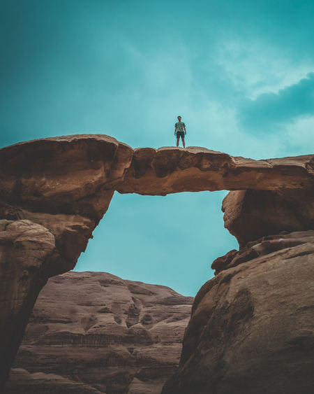 Low angle mid distance view of man standing on rock formation against sky
