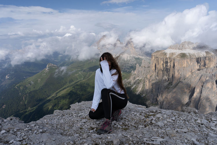 Full length of woman crouching at cliff against mountains