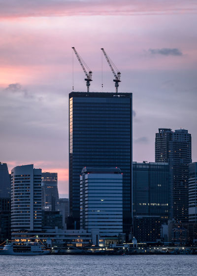 Cranes in city against sky during sunset