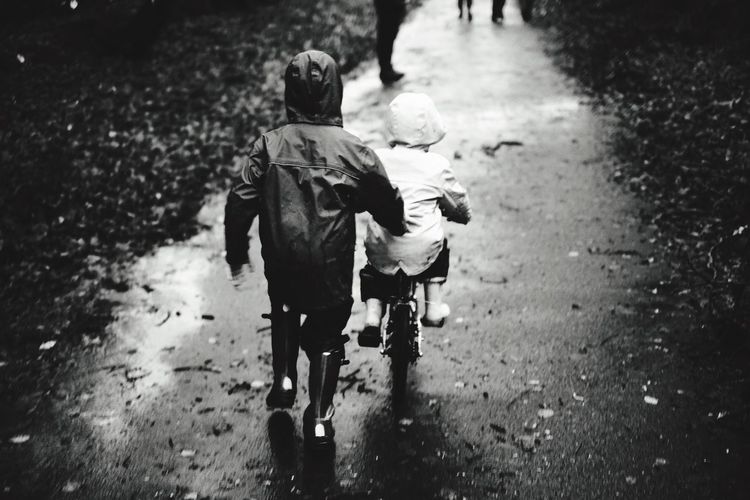 Rear view of child assisting sibling while cycling on road