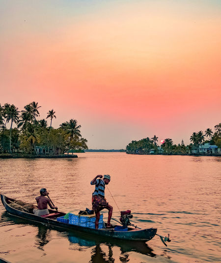 Fishermen in boat on lake against clear sky during sunset