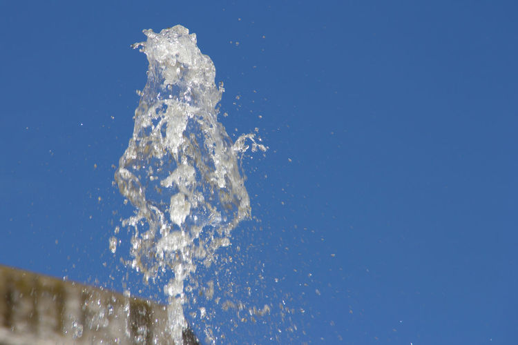 Low angle view of splashing water against clear blue sky