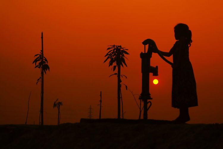 Silhouette woman photographing on field against orange sky