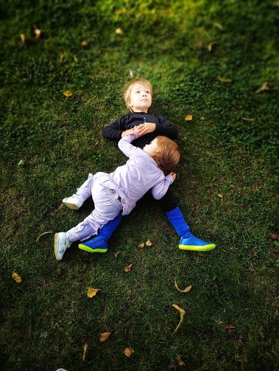 Full length of two little brothers sitting on grassy field
