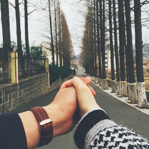 Cropped image of couple holding hands on road
