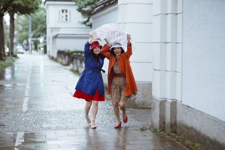 Surprised female tourists holding city map over head while running during rain