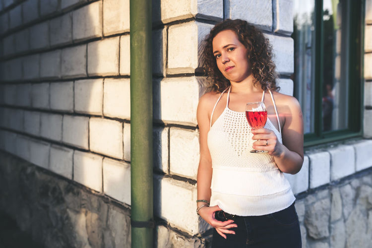 Portrait of woman having red wine against house