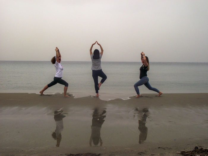 Friends doing yoga at beach against clear sky